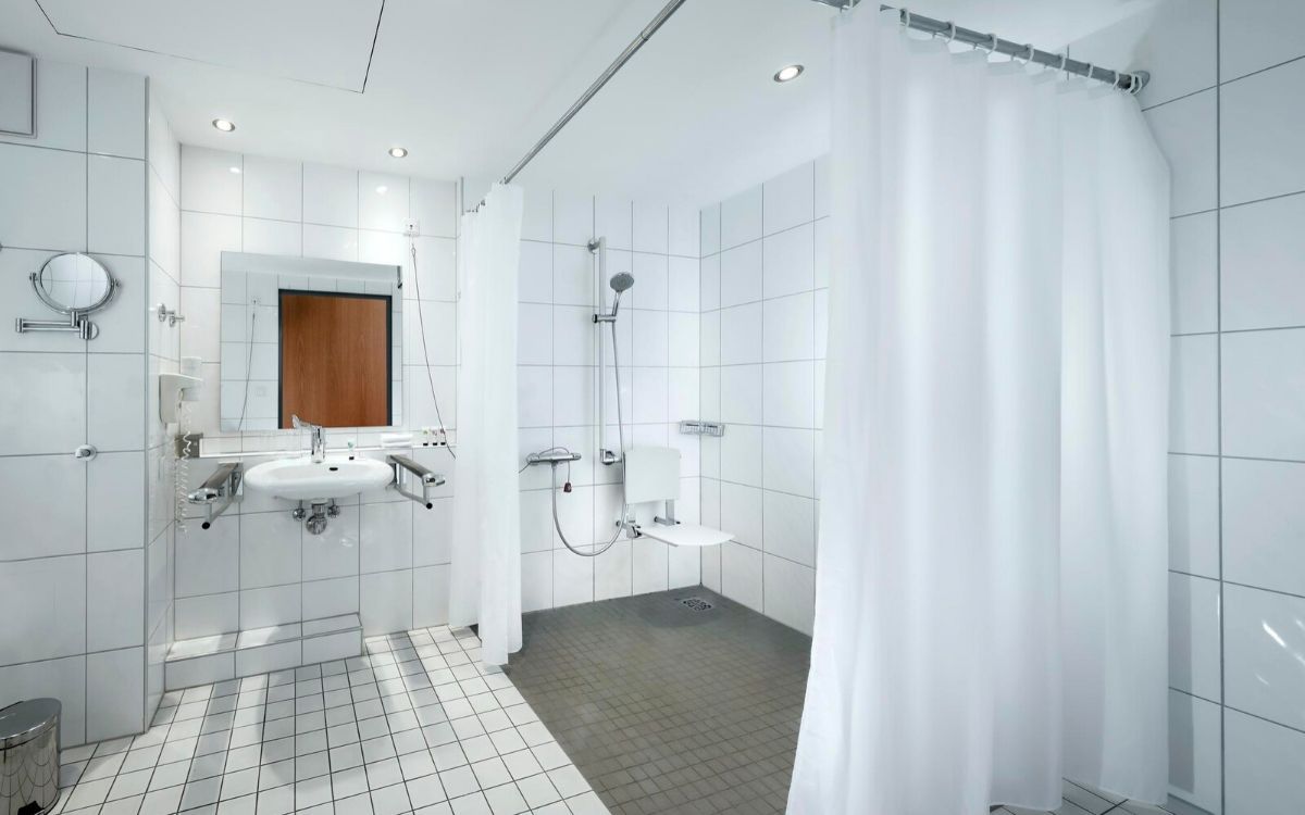 adapted bathroom with a wheel-in shower, wall mounted shower chair and grab rails
