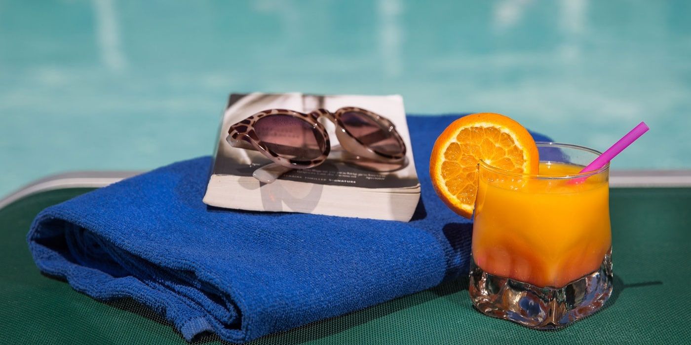 orange cocktail sitting poolside next to a good book