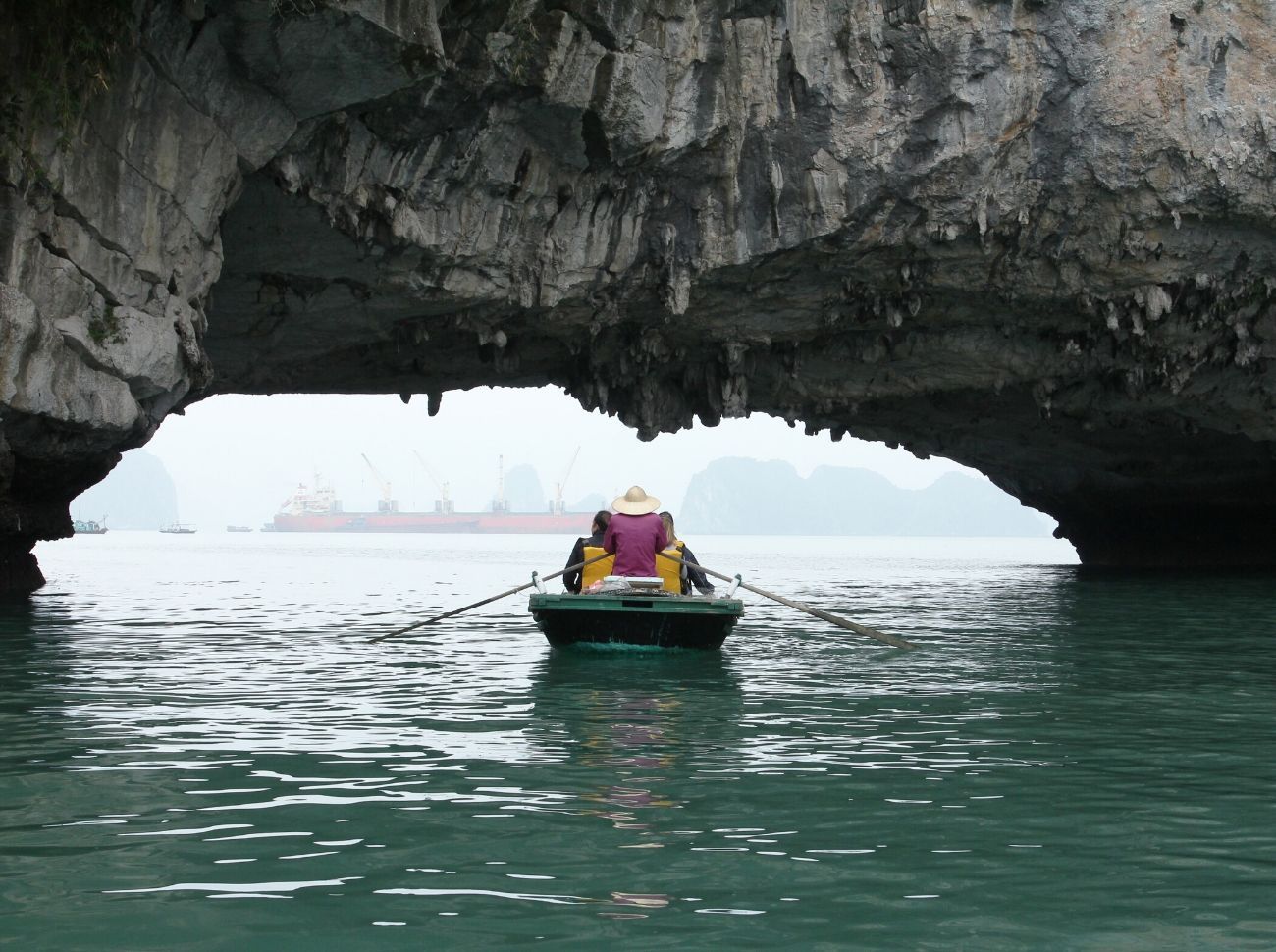 boat sailing under a cliff face in Halong Bay